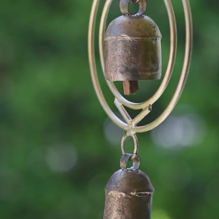 Close-up of a rustic wind chime of recycled tin and iron coated in copper with two bells with the text "hear the wind and think of me"