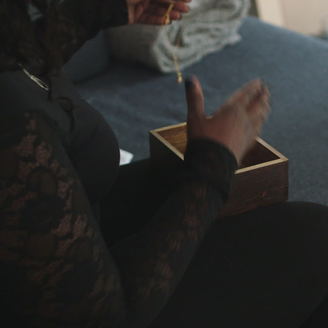 A video of a woman putting a necklace and handkerchief into a wooden memory box.