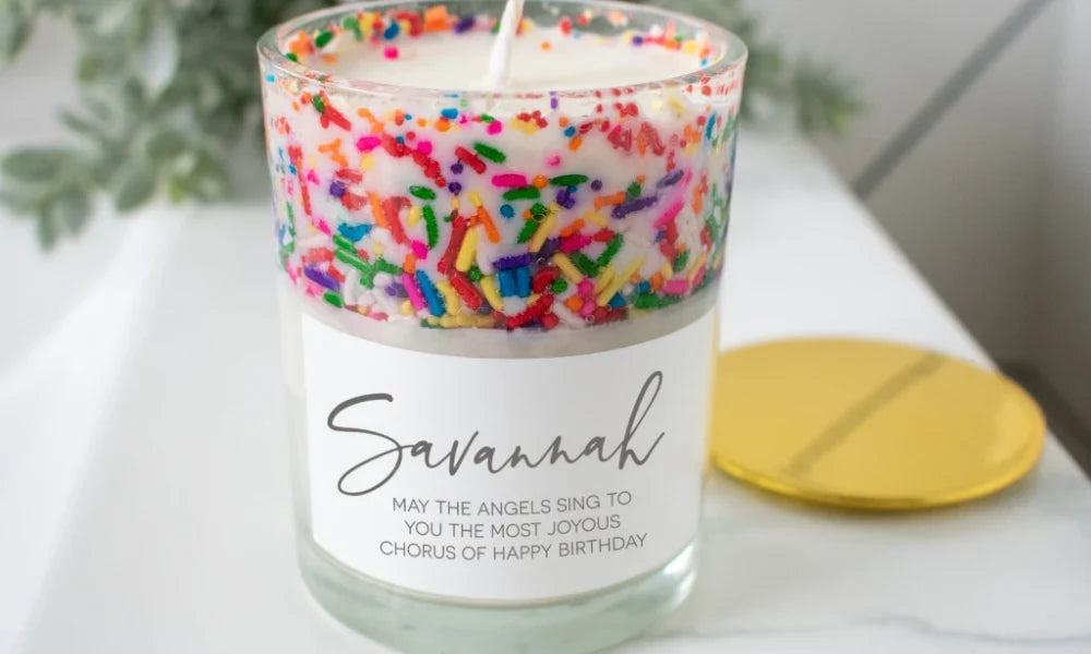 White candle with colorful sprinkles, glass jar, gold lid, personalized label saying 'Savannah', tribute for milestone birthday.