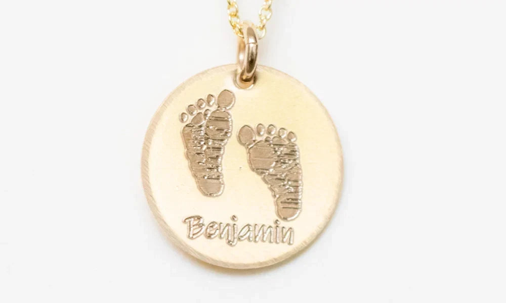 Custom memorial necklace with engraved baby footprints and the name 'Benjamin' in a circular gold pendant.