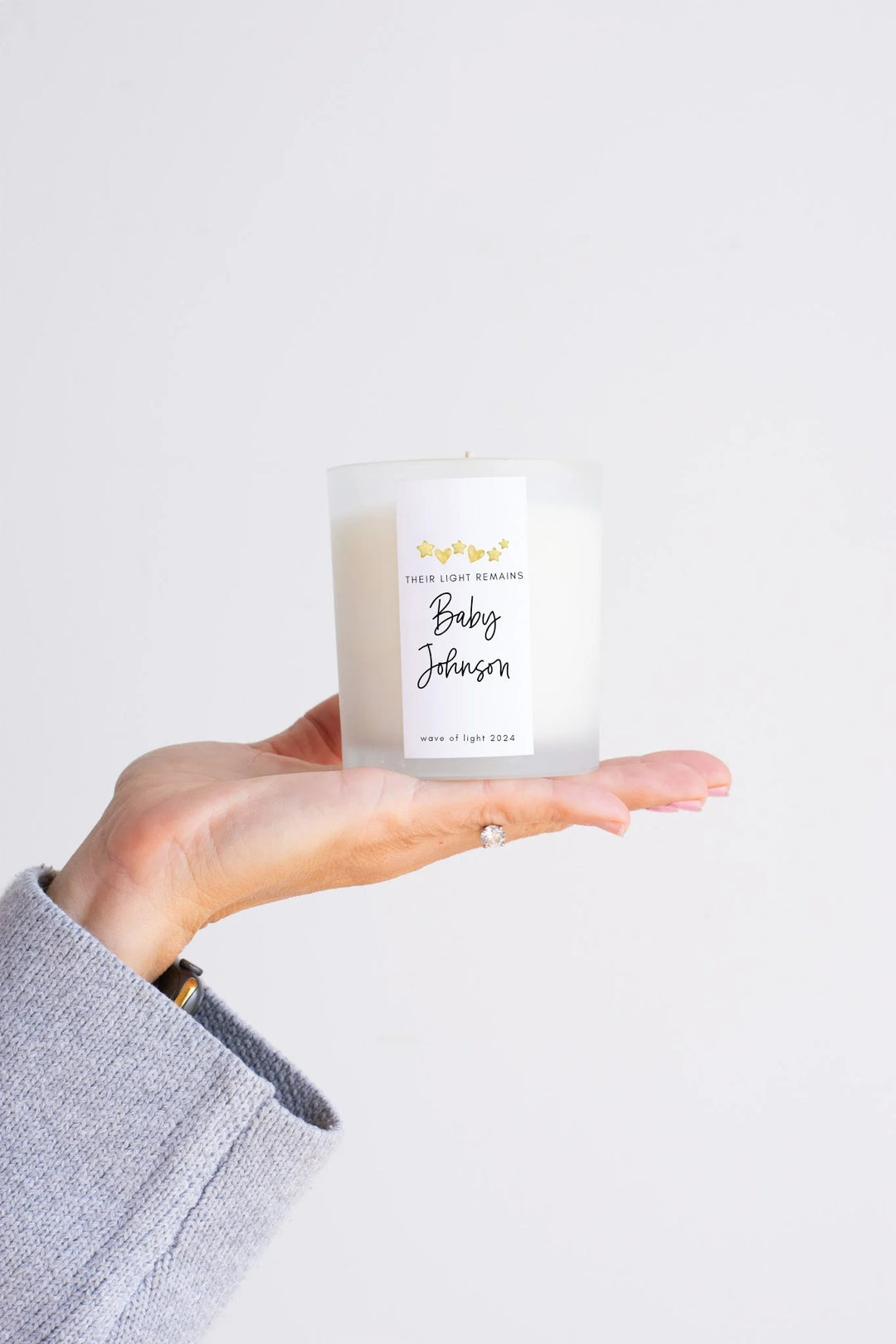 Frosted glass candle held in hand, with a white label reading 'Their Light Remains Baby Johnson', a remembrance gift, 14 Thoughtful Miscarriage Gifts That Actually Help.