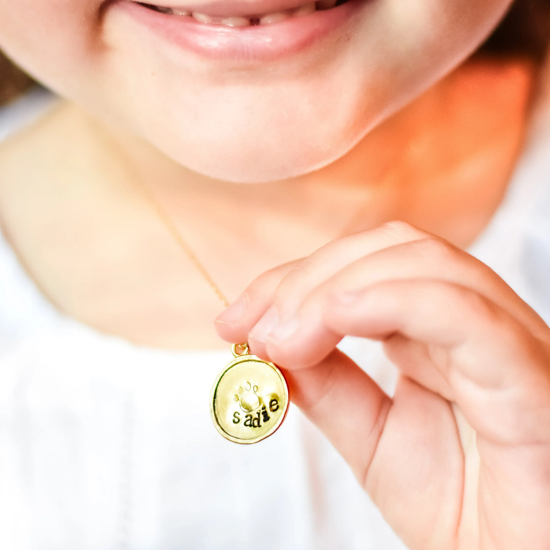 Gold oval pendant with the name 'Sadie' engraved on it, held up by a child, symbolizing pet remembrance. Losing a Pet: Our Story.
