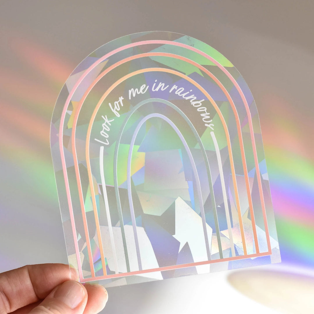 Giving a Little Light, a clear rainbow-shaped acrylic piece with pastel outlines and the text "look for me in rainbows".