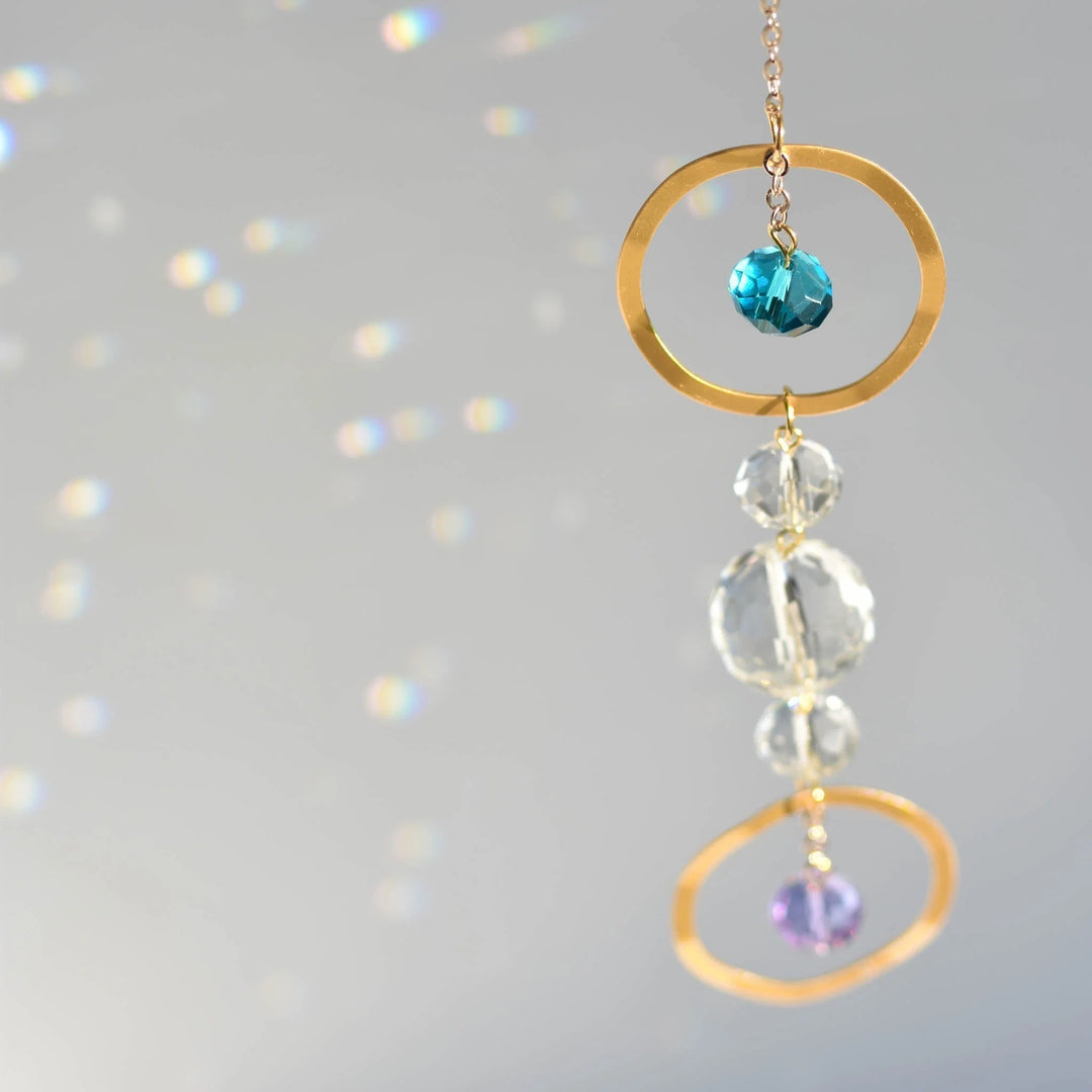 Gold and crystal jewelry featuring blue, clear, and purple beads, representing a remembrance gift, focusing on light reflection.