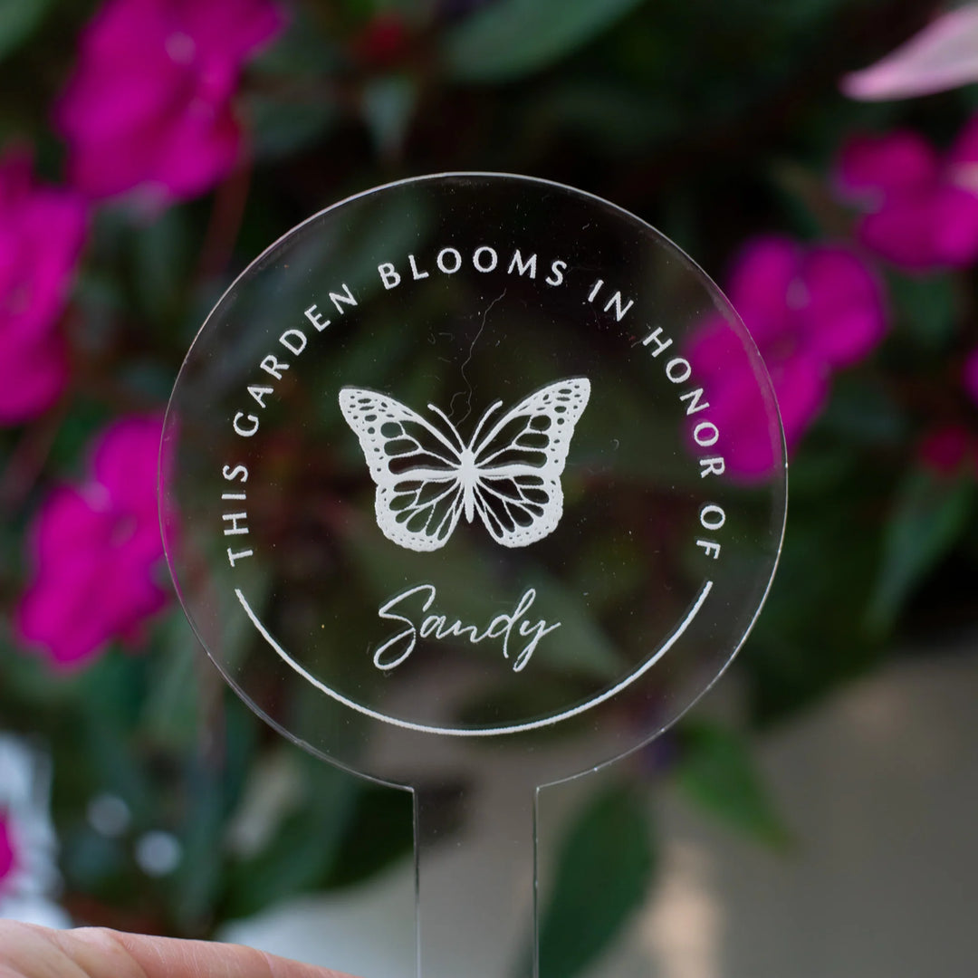 Clear acrylic garden marker with butterfly engraving, reads 'THIS GARDEN BLOOMS IN HONOR OF Sandy', for Gardening and Grief.