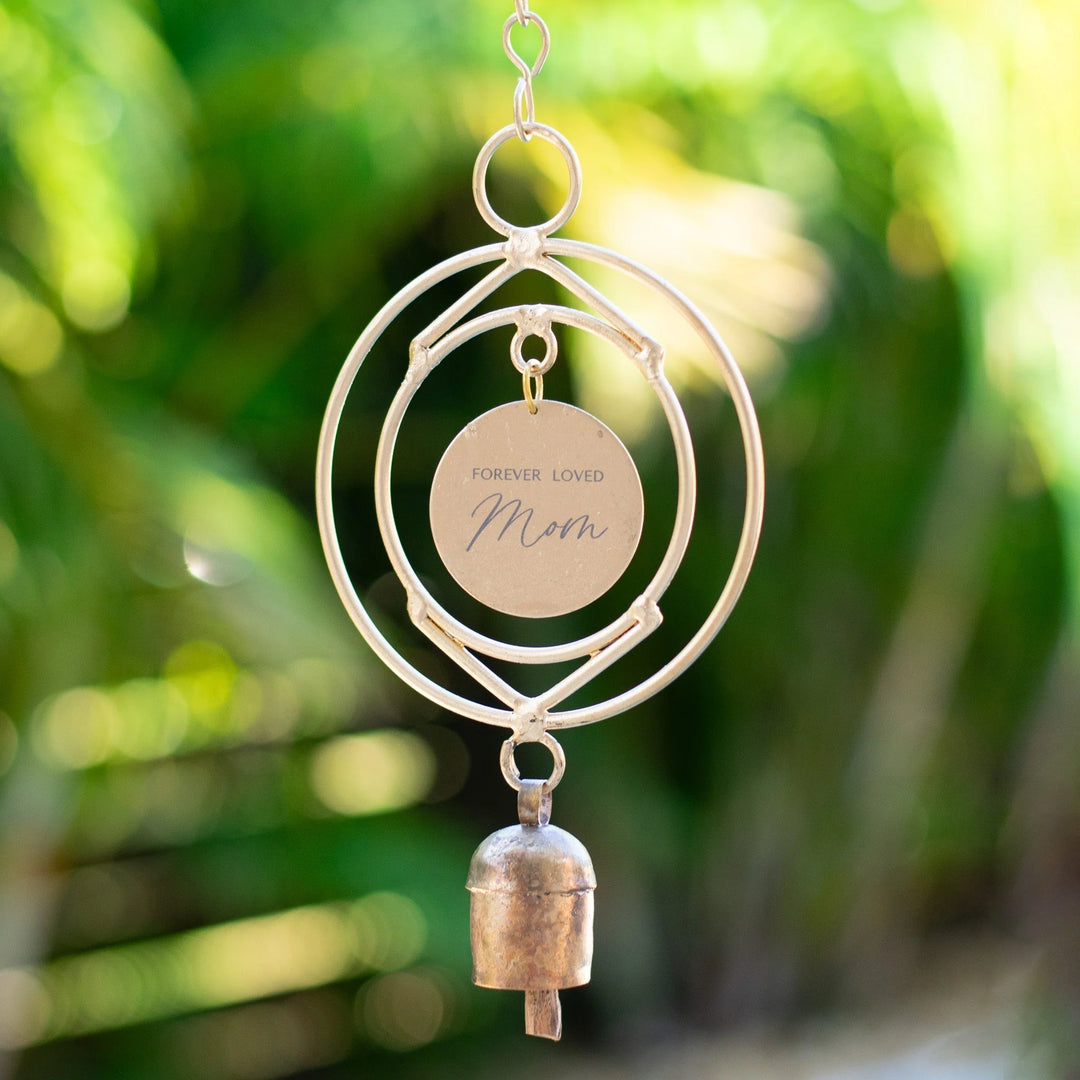 Memorial wind chime featuring a gold circular tag engraved 'Forever Loved Mom' with a small bronze bell, hanging outdoors.