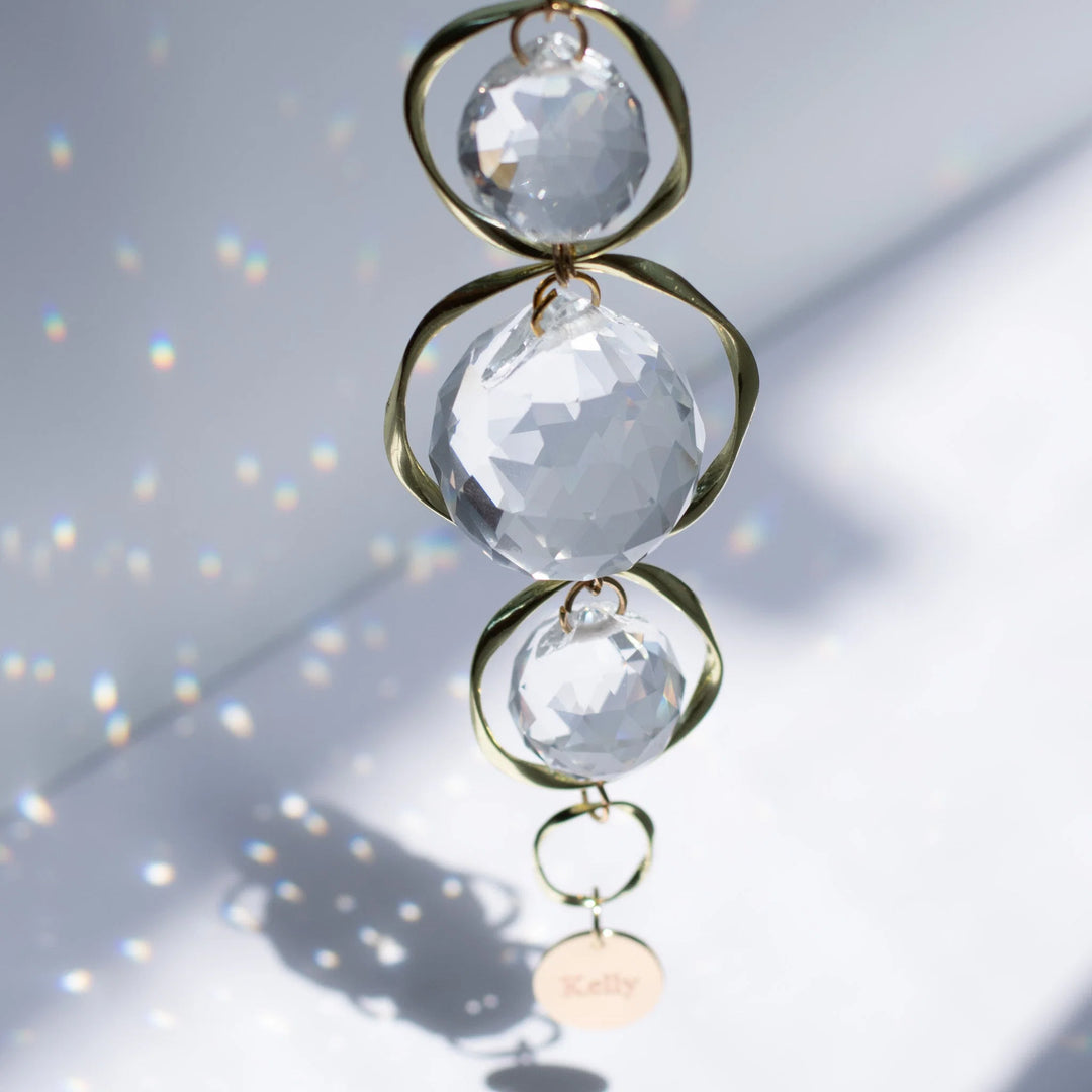 Memorial Suncatchers & Rainbow Makers: A Thoughtful Guide. Crystal suncatcher with three clear glass orbs and gold loops.