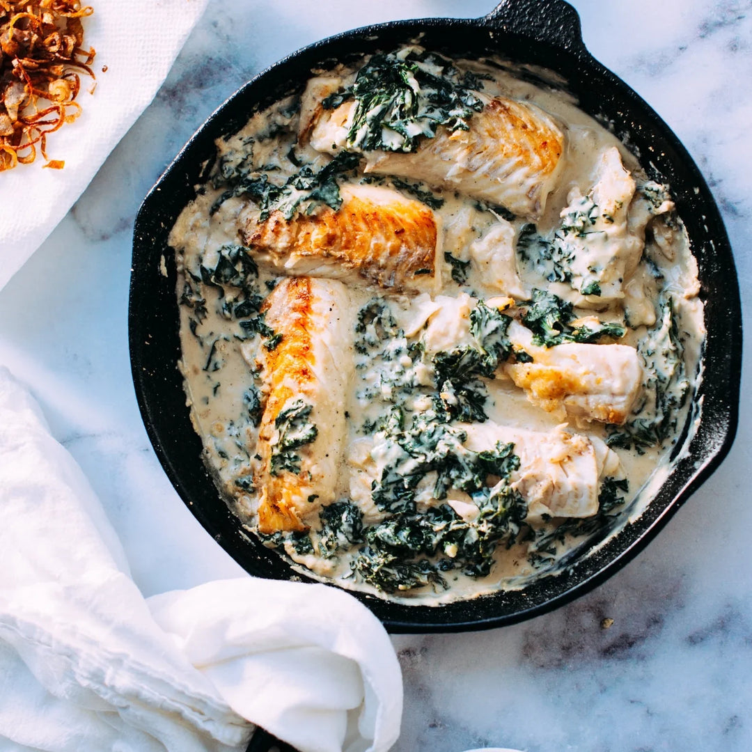 9 Tips for Bringing Meals to Grieving Families - cast iron skillet with creamy fish and spinach, garnished with herbs.