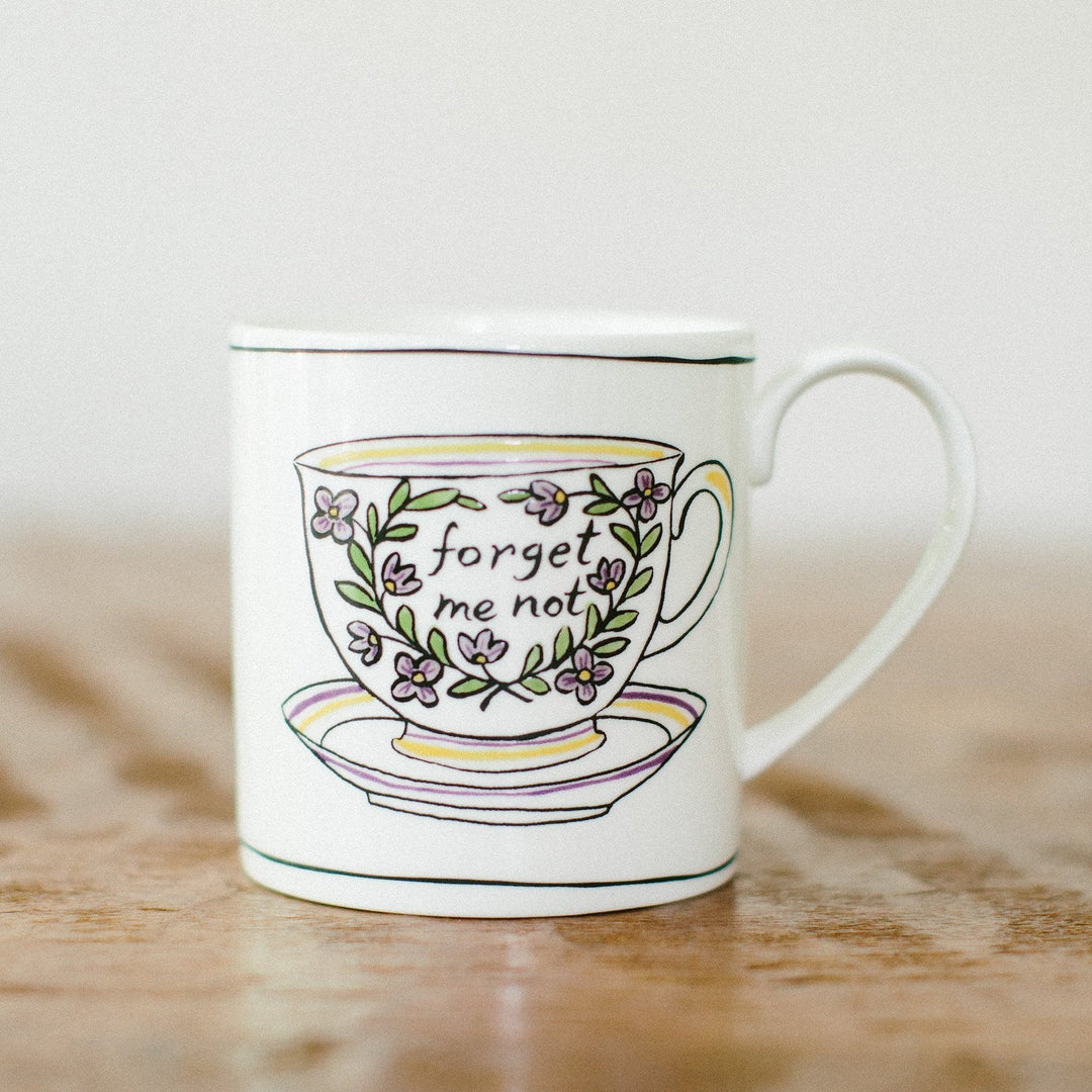 A white ceramic mug that says "forget me not" with purple floral sprigs