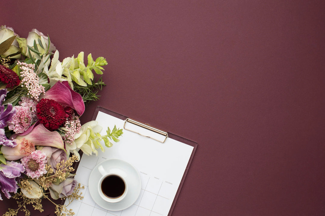 Floral arrangement with purple and red flowers beside a white coffee cup on a clipboard with blank calendar pages. The Art of Thoughtful Gift Giving.
