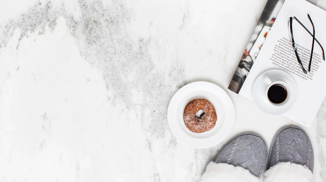 Goals to Make While Grieving: Gray slippers on marble surface with a donut, coffee cup, and a book.