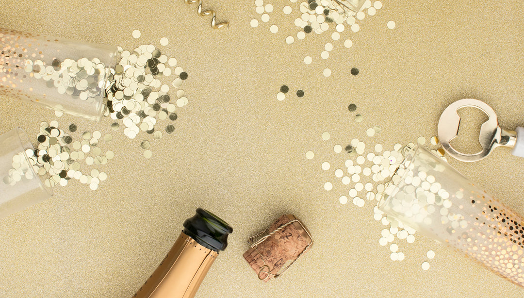 Bringing in the New Year While Grieving: Champagne bottle, cork, and scattered gold confetti on a glittery background.