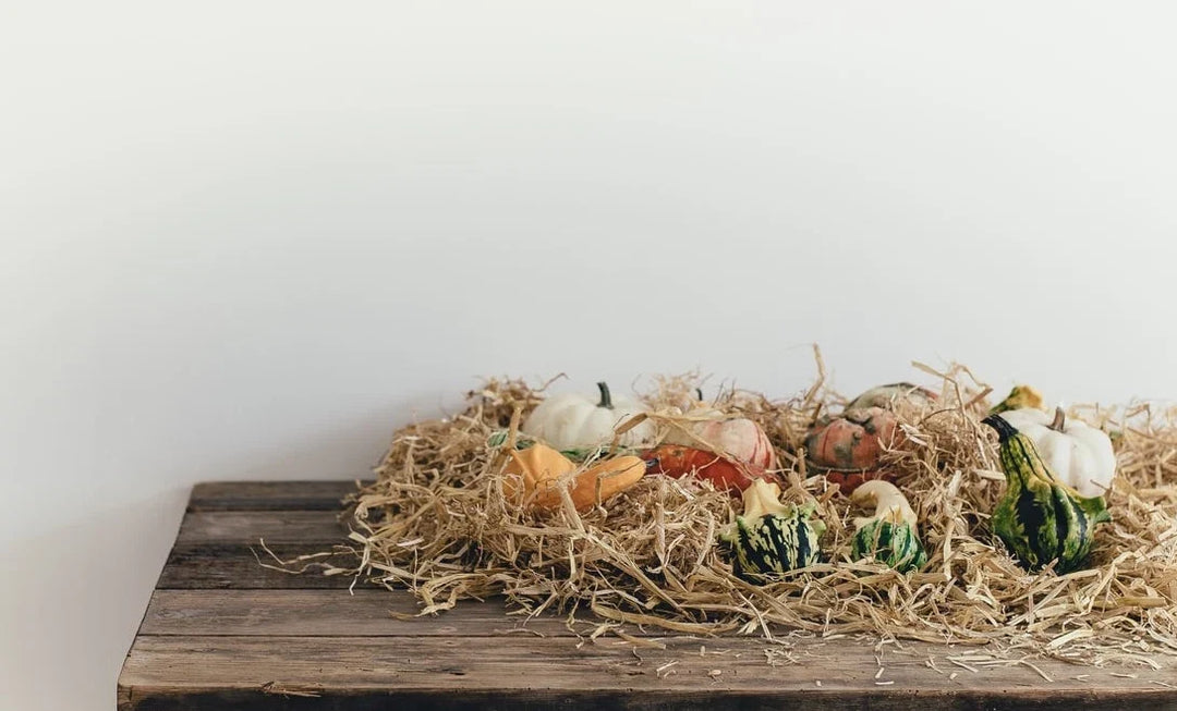 Assorted pumpkins and gourds in various colors resting on straw on a wooden table, creating a seasonal display.