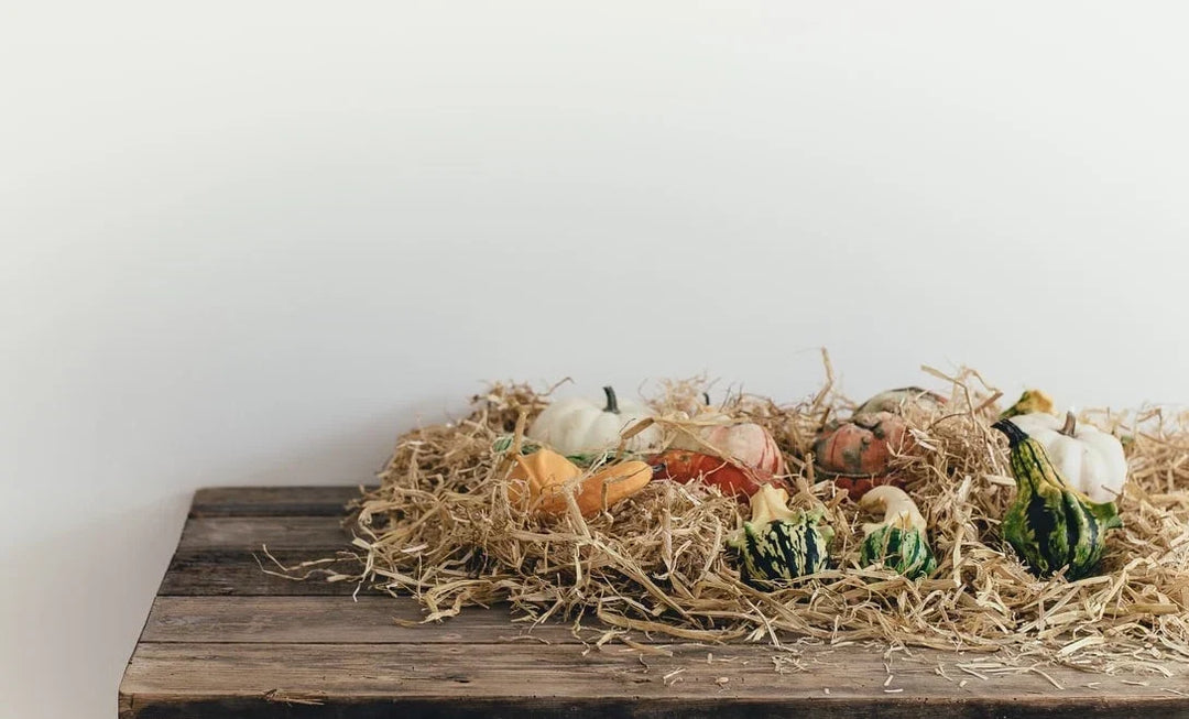 Assorted pumpkins and gourds in various colors resting on straw on a wooden table, creating a seasonal display.