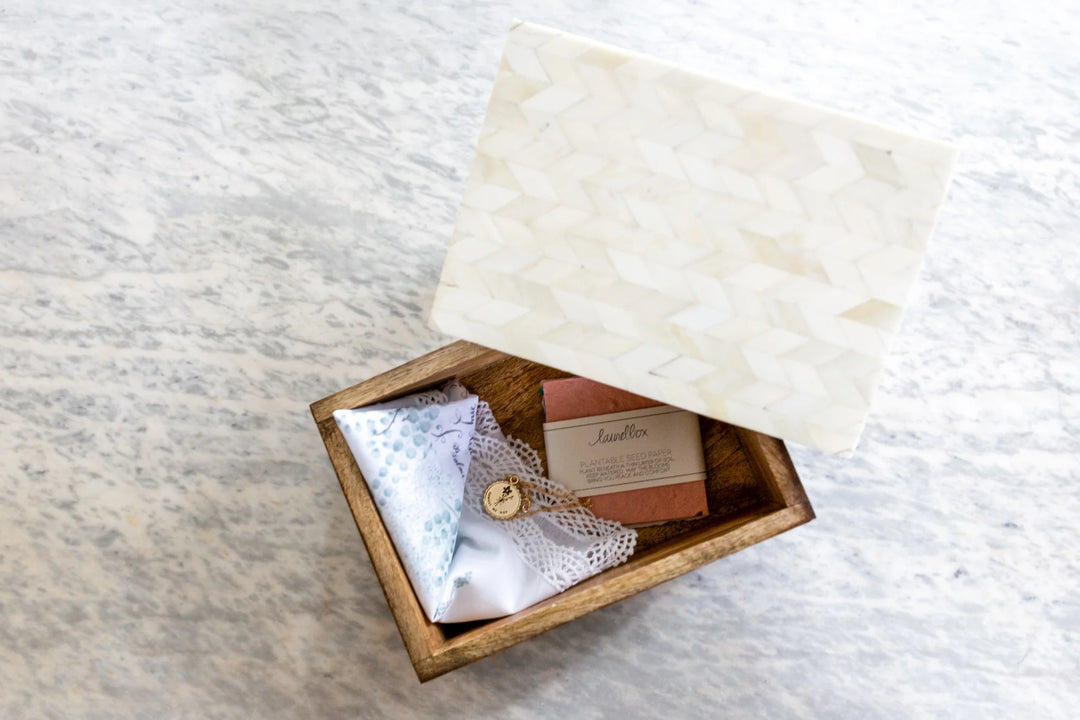 Wooden keepsake box with a white patterned lid, containing a fabric parcel and seed paper, relevant to memorial keepsake.