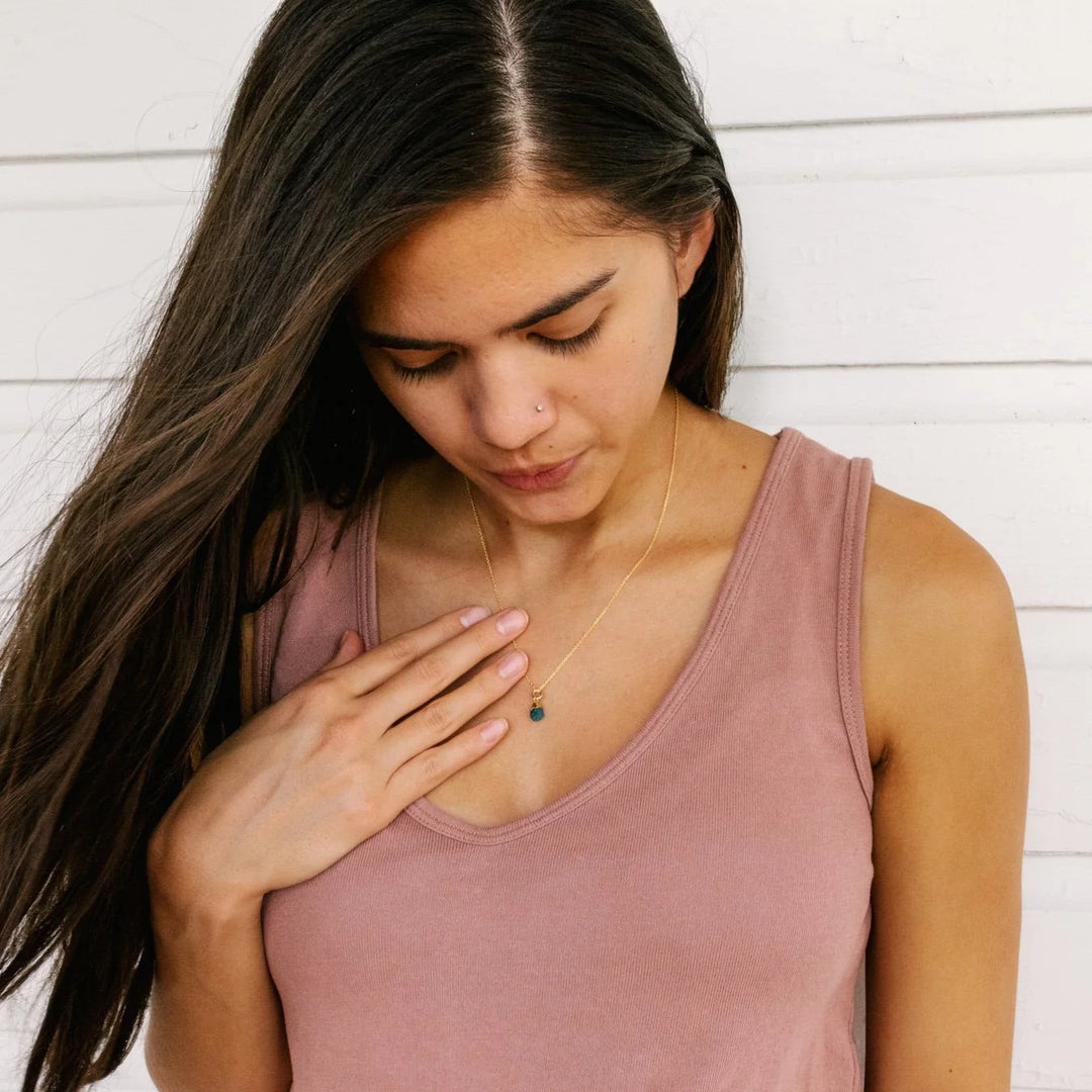 Woman wearing a gold necklace with a small blue gemstone pendant, showing care for her memorial keepsake jewelry.