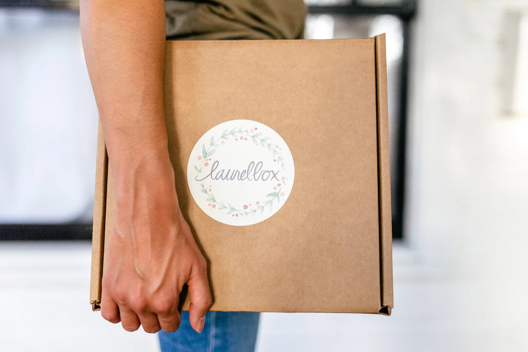 Brown cardboard box with a round label showing the name 'launellox' and floral design, held in a person's hand.