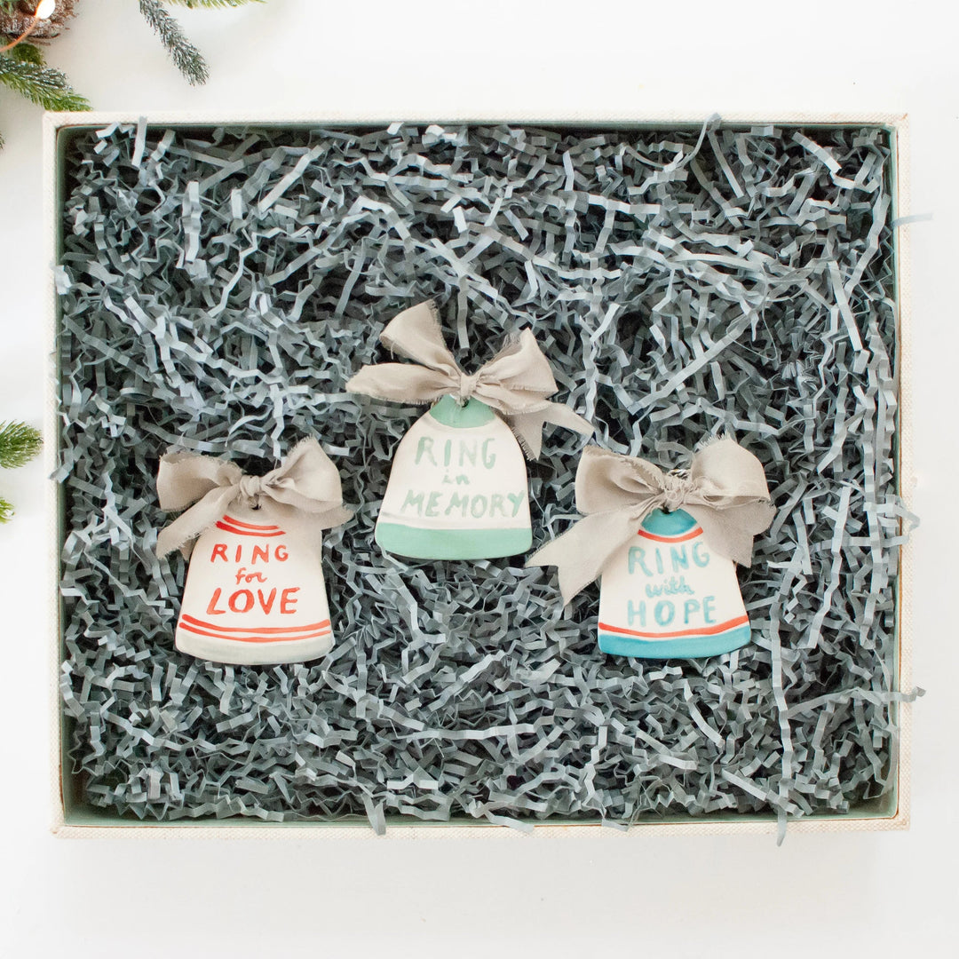 Three ceramic bells in a gift box, with tags: 'Ring for Love', 'Ring in Memory', 'Ring with Hope'. Decorated with beige ribbons.