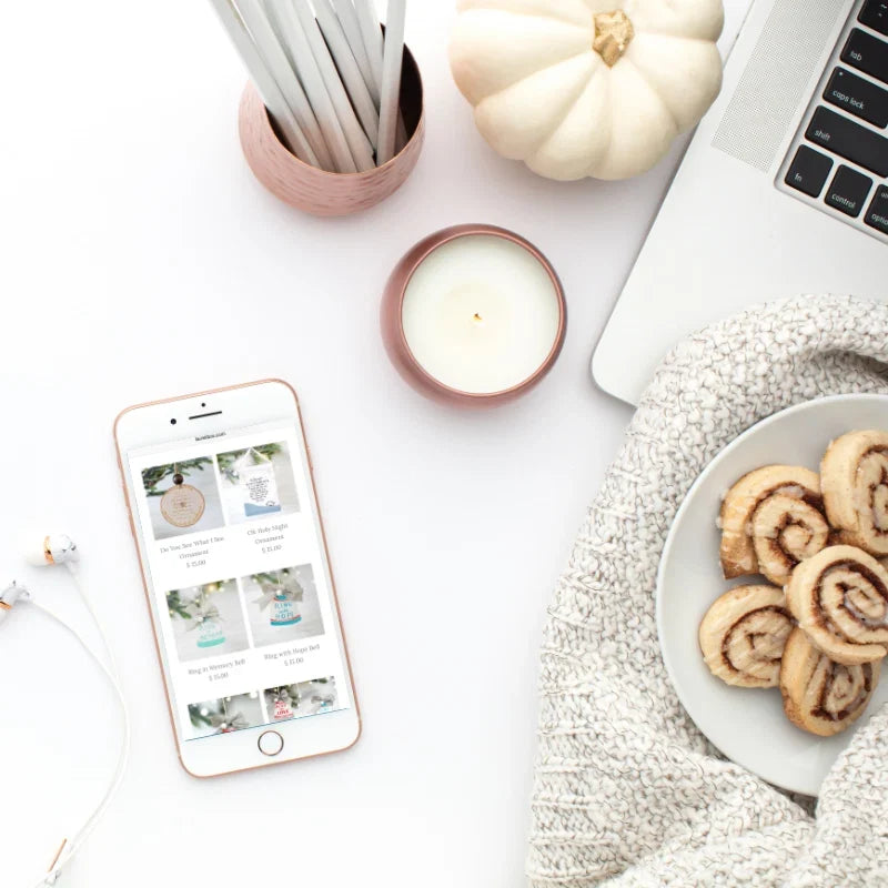 Flat lay of a phone showing gift options, candle, pumpkin, plate with cinnamon rolls, and a laptop. Giving Thanks When All Is Dark.
