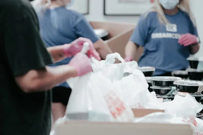 Volunteers wearing gloves and masks are packing meal containers into bags at a charity event for Volunteerism: Service as Grief Support.