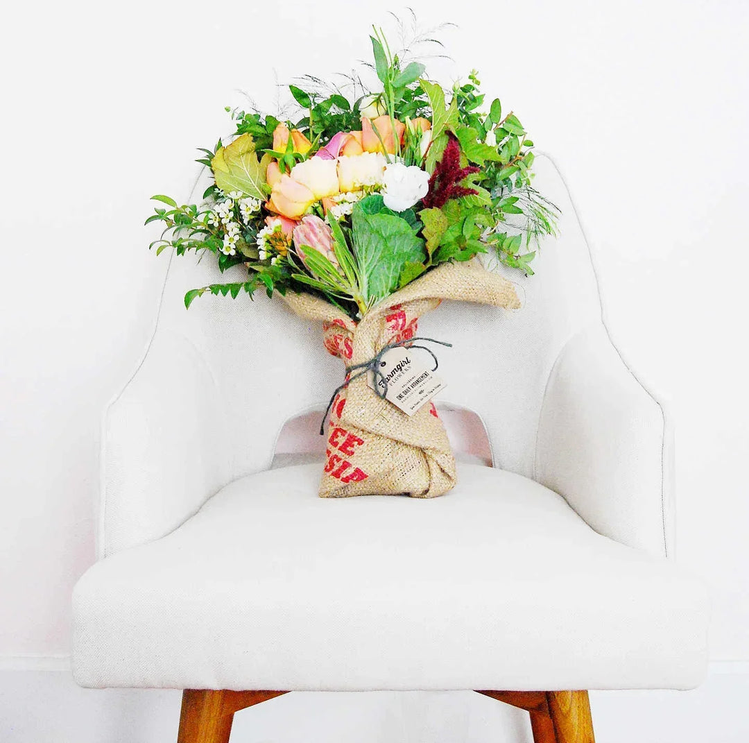 Bouquet of mixed flowers in burlap wrapped with twine, placed on a white upholstered chair.