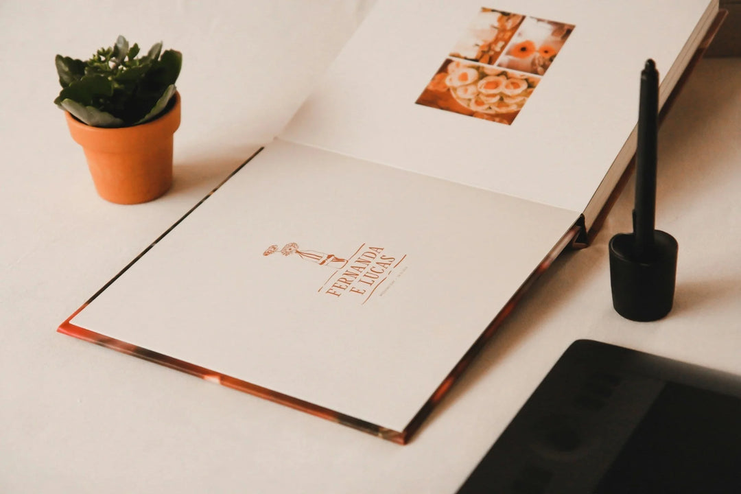 Open photo book with white pages, featuring a logo in gold. Small green plant in a terracotta pot nearby. 20 Meaningful Gifts for the Loss of a Spouse or Partner.