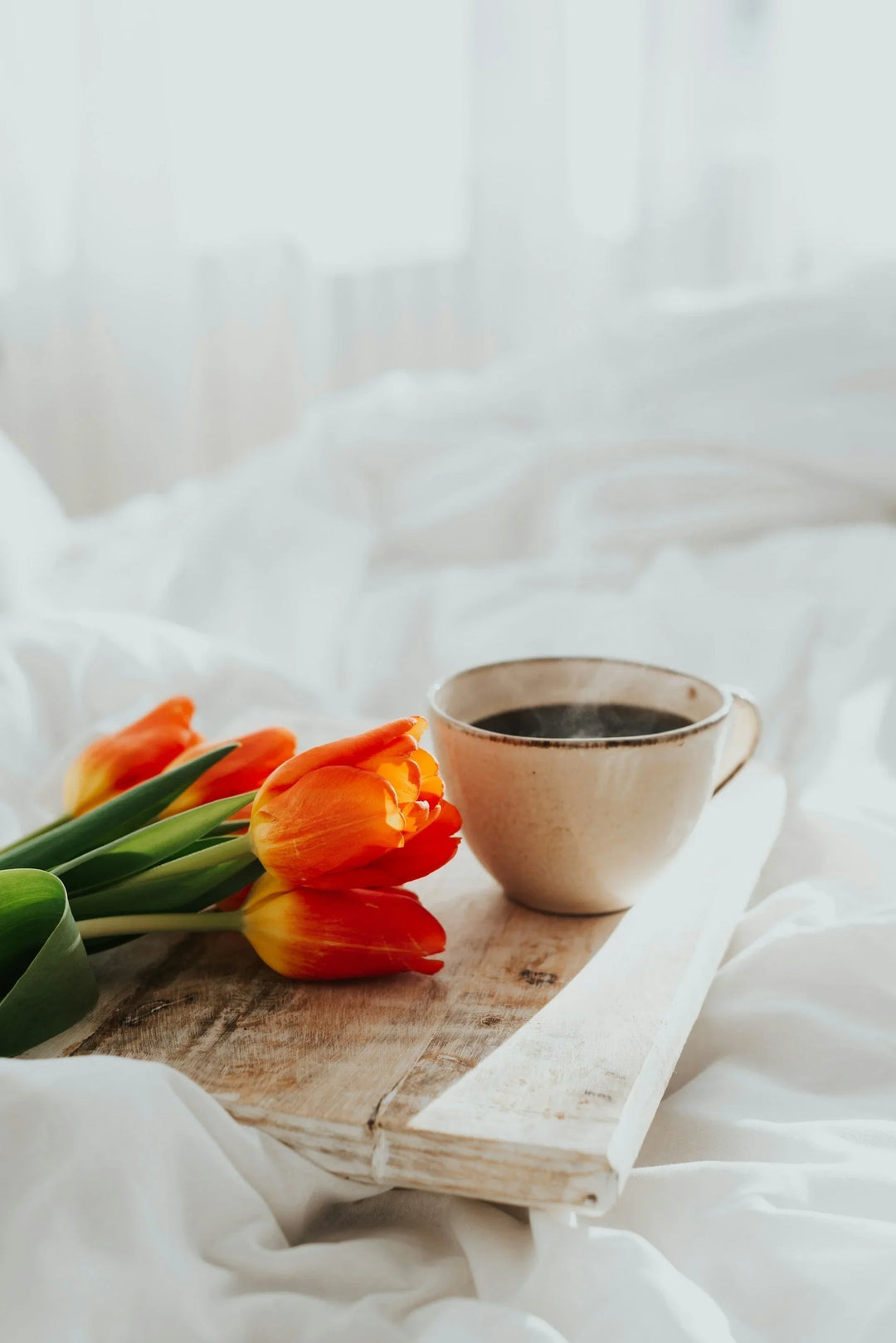 Grief-Sensitive Morning Routine with orange tulips and a beige ceramic cup with coffee on a wooden tray.
