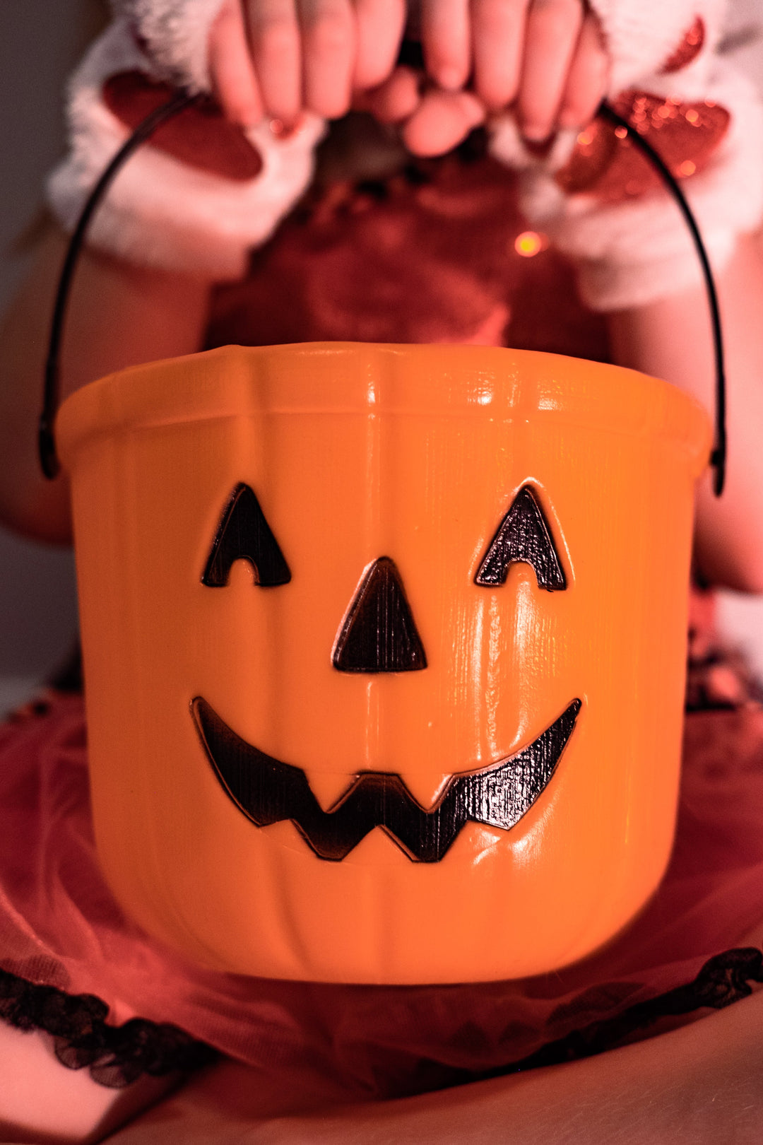 A set of hands holding an orange bucket with a smiling face of a pumpkin.