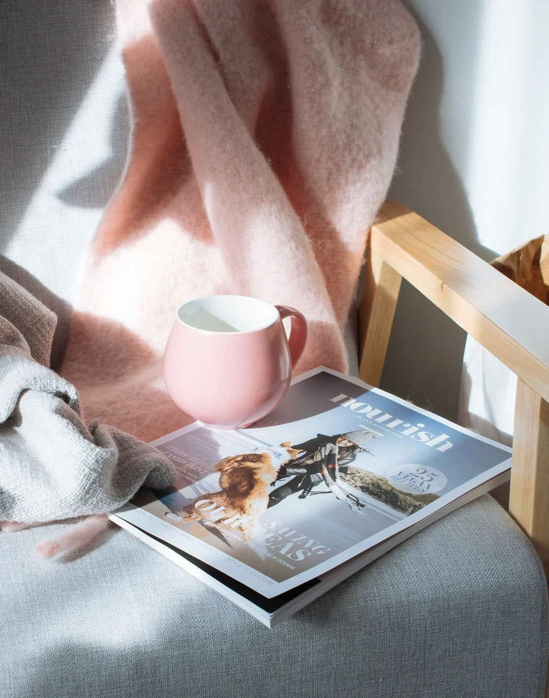 Setting New Year’s Resolutions That Include Self-Care: a pink ceramic mug beside a magazine on a chair with a soft blanket.