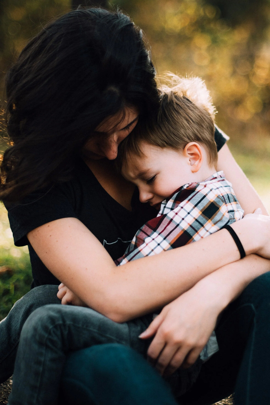 Woman in a black shirt holds a young boy in a plaid shirt, both with eyes closed, during Children’s Grief Awareness Month.