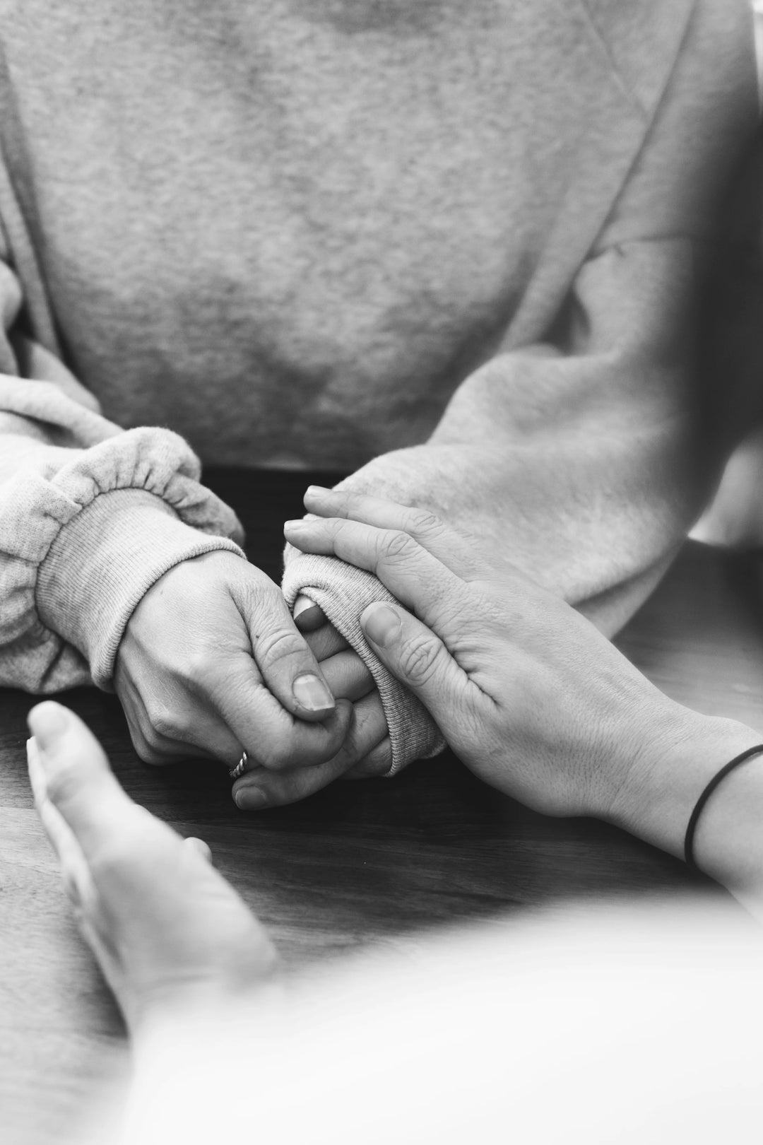 Hands of two people holding each other, one wearing a light gray sweatshirt, conveying support. How to Support a Grieving Long-Distance Partner or Friend.