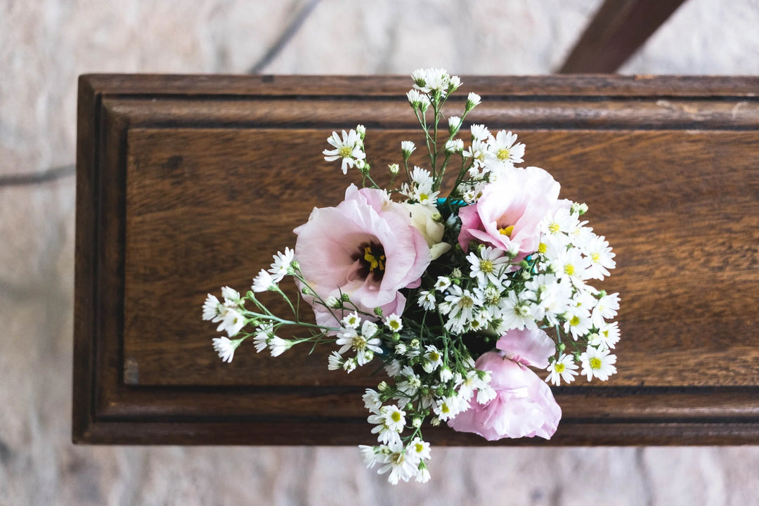 A bouquet of pale pink flowers and small white daisies on a wooden table, representing sympathy gifts. Funeral Gifting Etiquette 101.