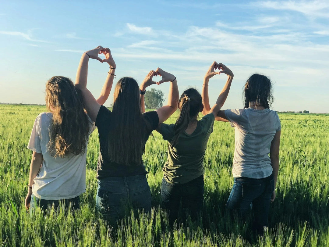 Four people standing in a green field forming heart shapes with their hands, representing support and friendship. Ways To Recognize Those Who Have Supported You Through A Diﬃcult Season.
