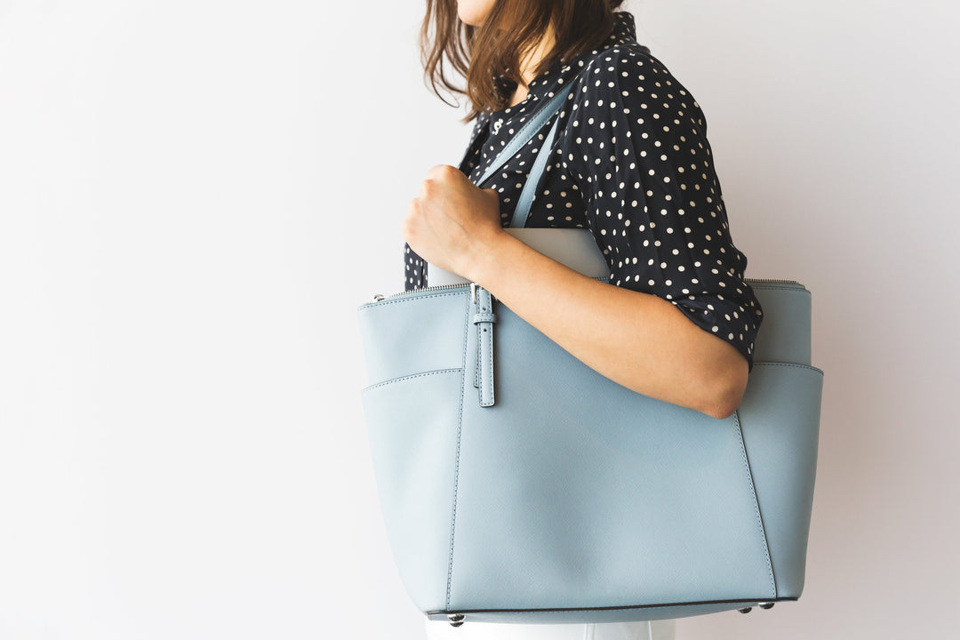 Woman with blue bag wearing a polka dotted shirt. Standing in front of a white wall background.