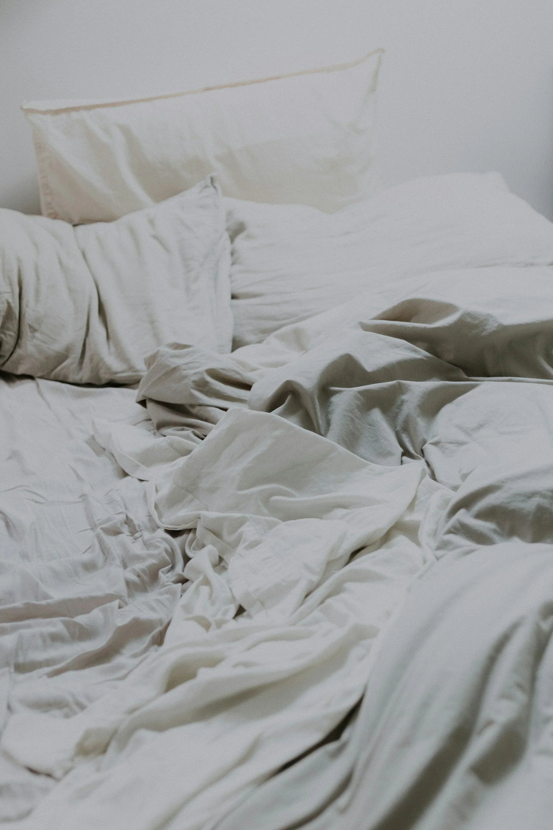 White bedding with wrinkled sheets and several pillows, emphasizing comfort linked to The Connection Between Grief & Sleep: Tips For Better Rest.