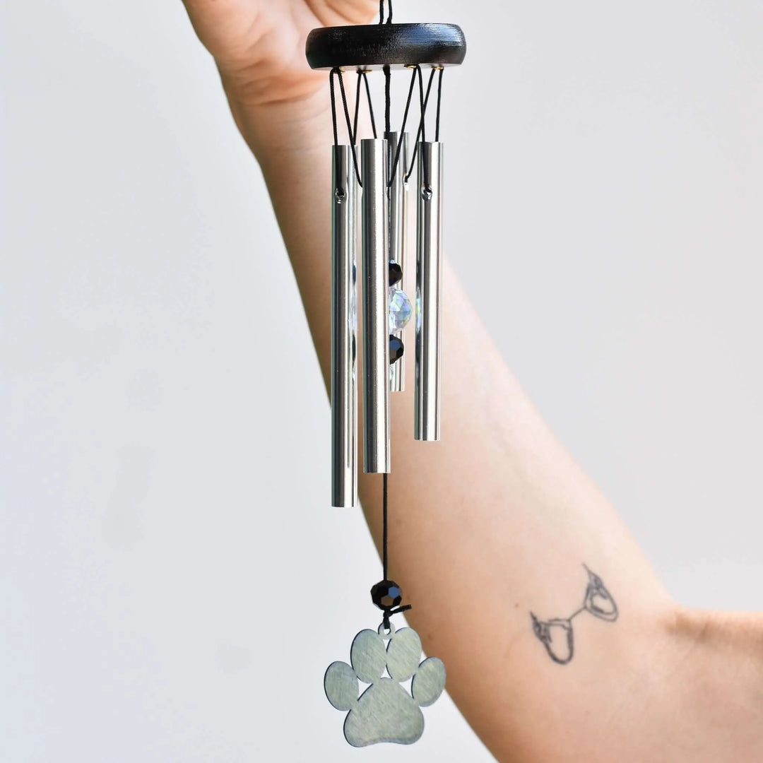 Pet Memorial Wind Chimes: 2026 Buying Guide. Hand holding black wooden top with silver tubes and paw print charm.