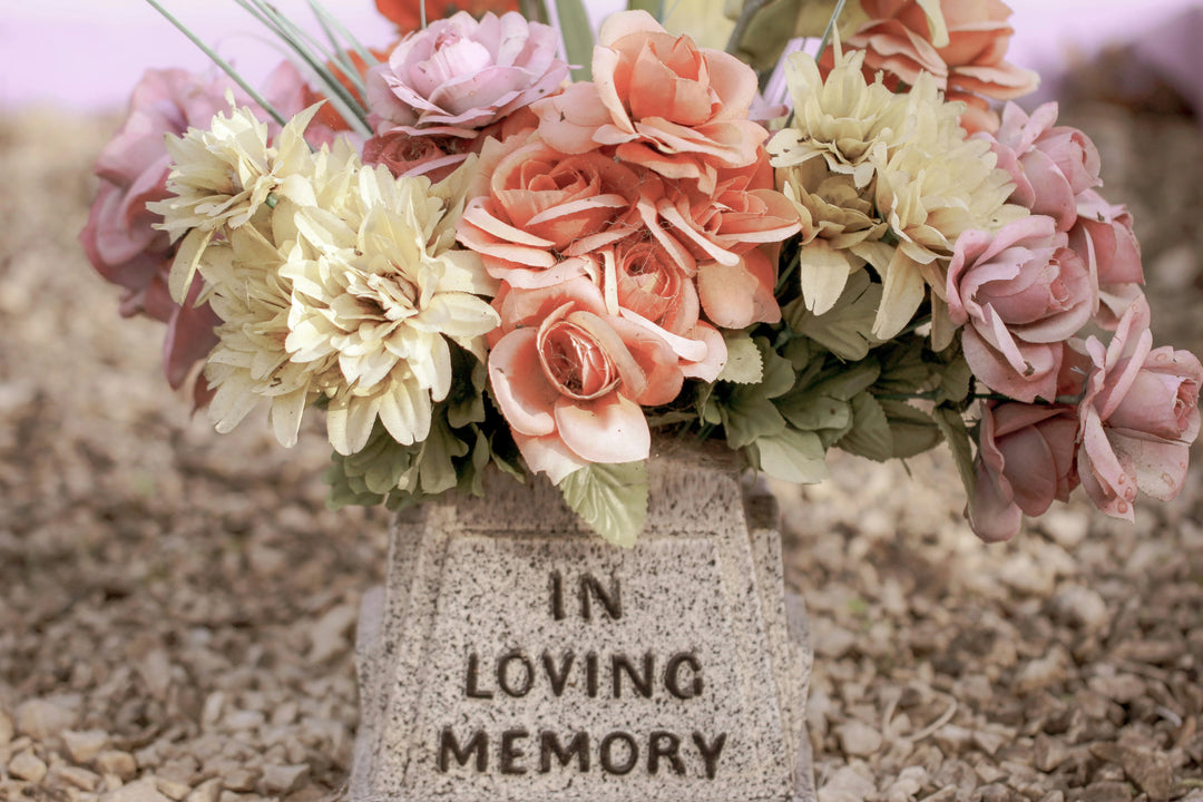 Artificial floral arrangement in shades of pink and yellow atop a stone base engraved with 'IN LOVING MEMORY', honoring a loved one.