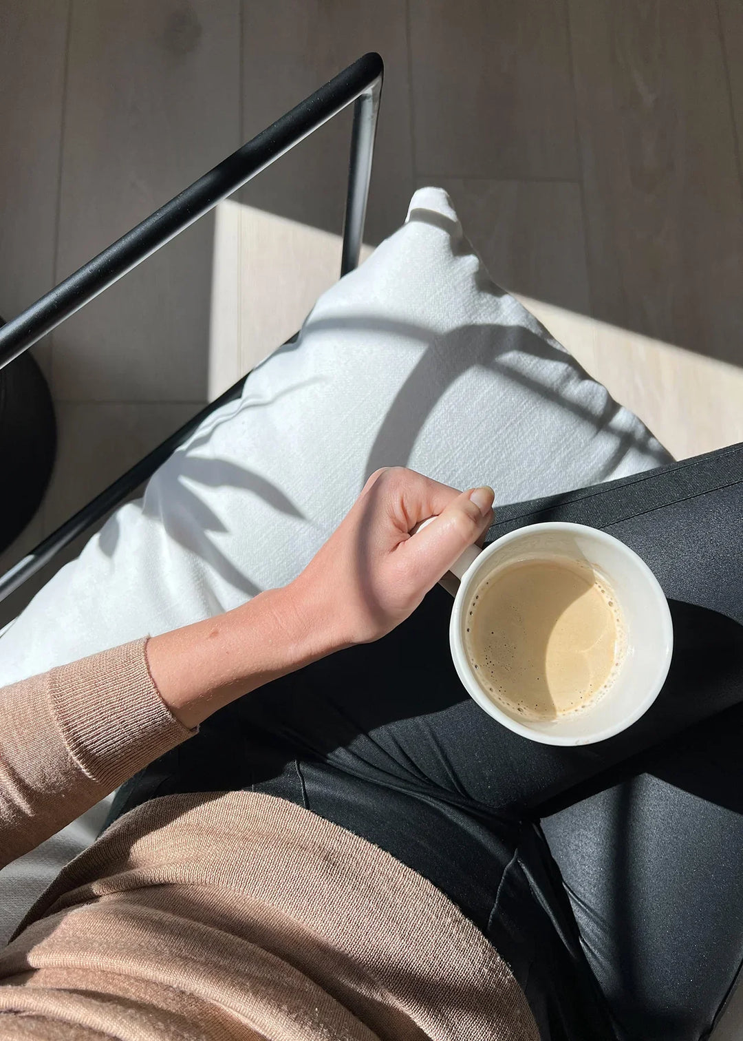 Being Seen in Grief by Meghan Riordan Jarvis, MA, LICSW. Hand holding white coffee cup, wearing beige sweater, sitting on white pillow.