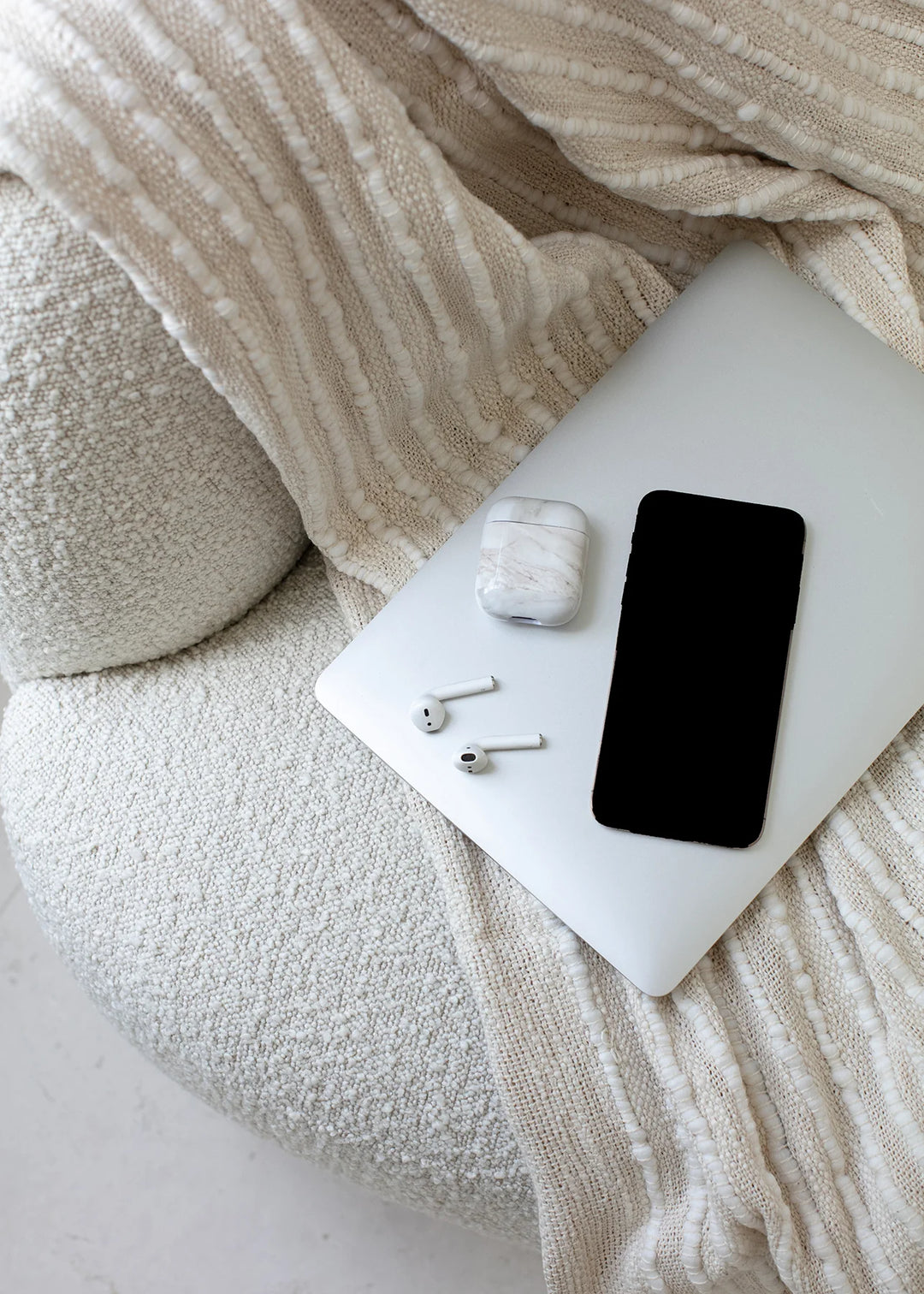 A smartphone, white earbuds, and a patterned case on a white blanket, representing Staying Connected: Using Technology to Send Condolence Gifts and Messages.
