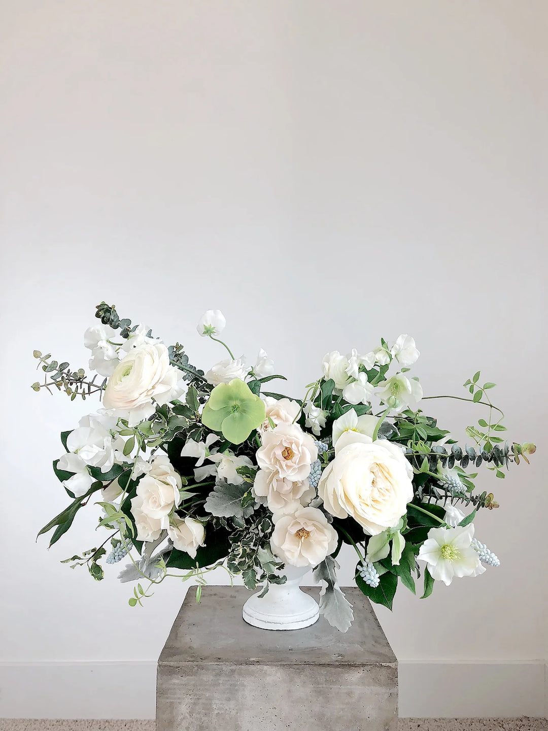 White and green artificial flower arrangement in a white pedestal vase, placed on a grey stone surface. How to Honor Loss on International Bereaved Mothers Day.