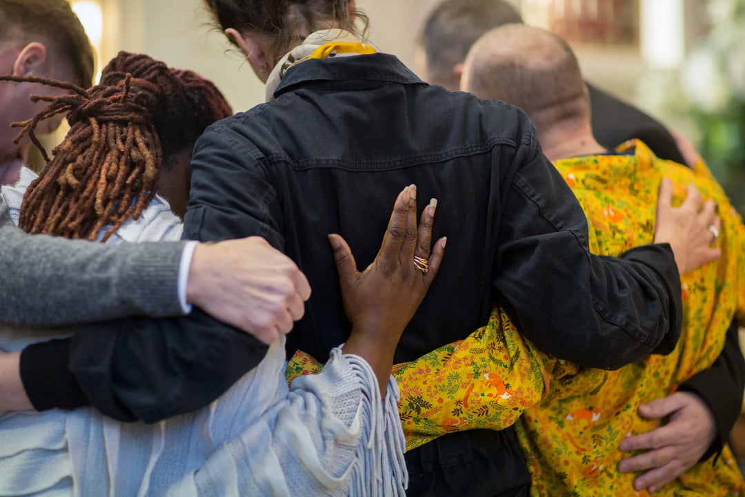Group of people embracing, wearing varied clothing colors, showing support in a moment of connection. How to Support a Friend in the Weeks and Months After a Loss.