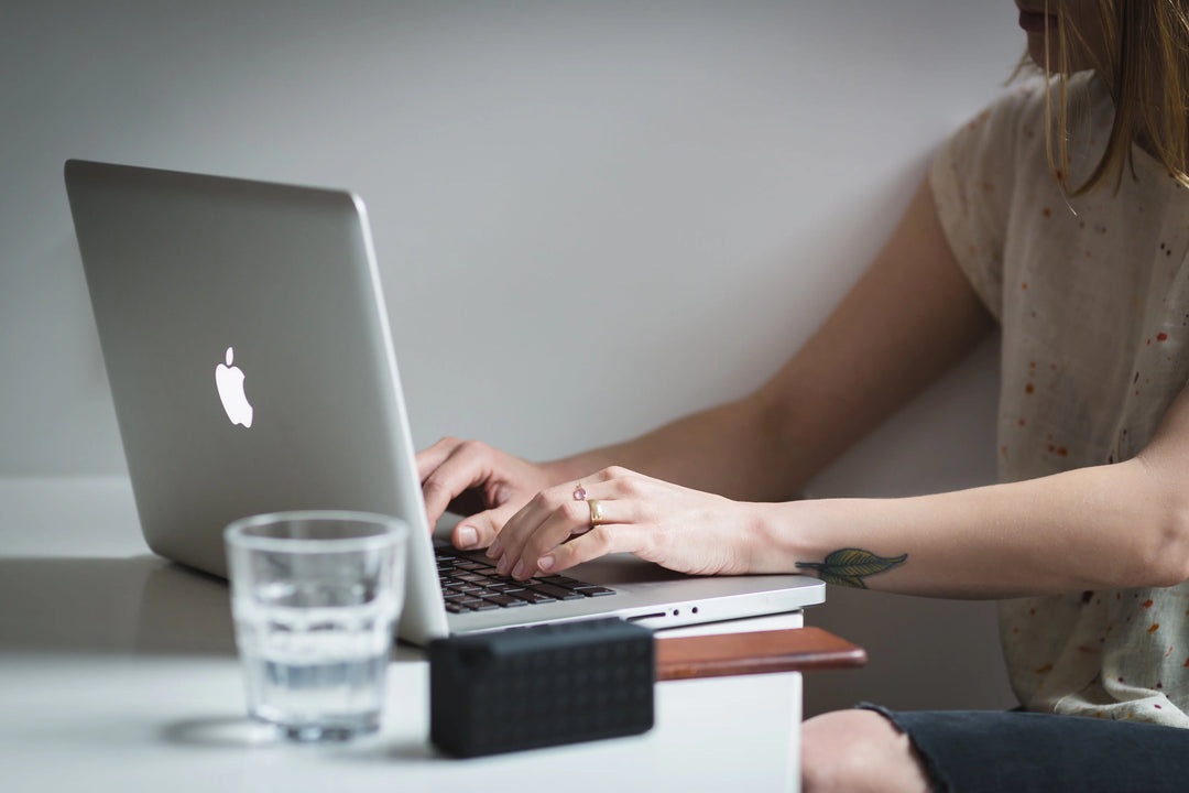Corporate Sympathy Gifts: 2026 Bulk Ordering Guide for HR. Silver laptop with Apple logo, hands typing, glass of water on table.