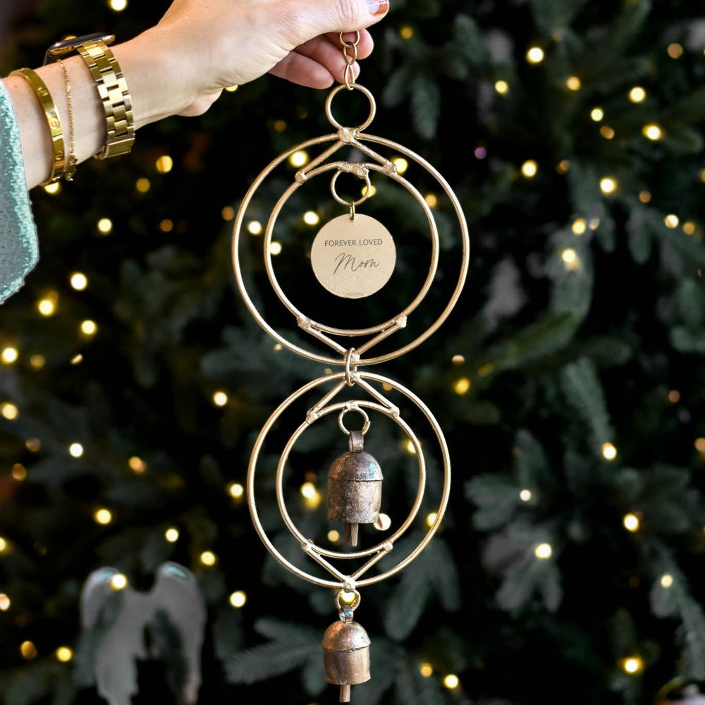 A wind chime with the name "Mom" engraved, being held in front of a tree.