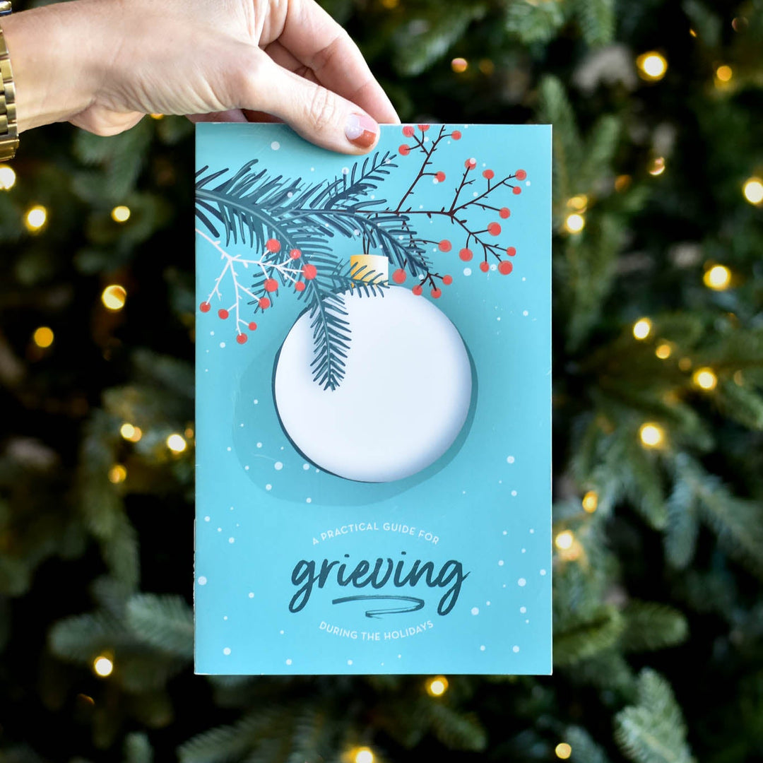 A Practical Guide to Grieving During the Holidays booklet held up, featuring a turquoise cover with snowflakes and holly.