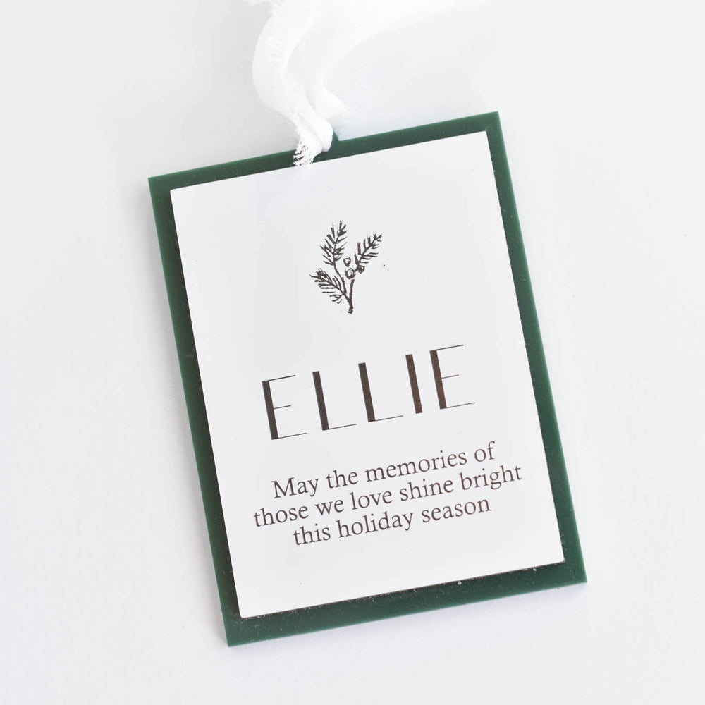 A Christmas ornament with a white background, dark green border, and a white hanging ribbon. The tag is personalized with the name 'ELLIE.'