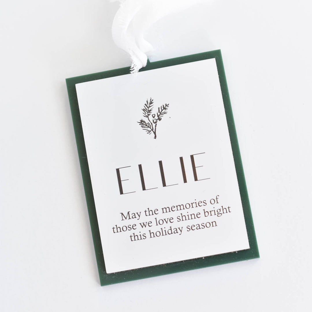 A Christmas ornament with a white background, dark green border, and a white hanging ribbon. The tag is personalized with the name &