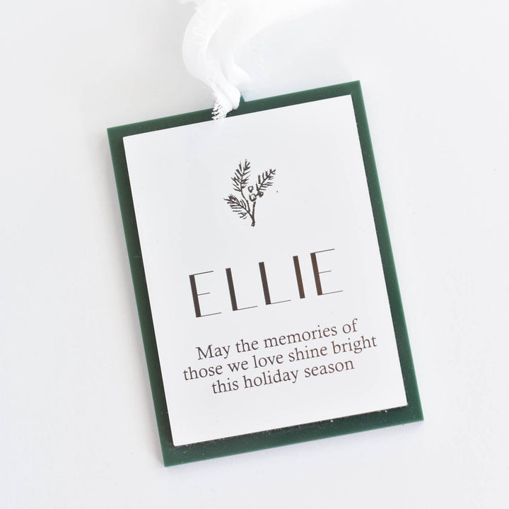 A Christmas ornament with a white background, dark green border, and a white hanging ribbon. The tag is personalized with the name &
