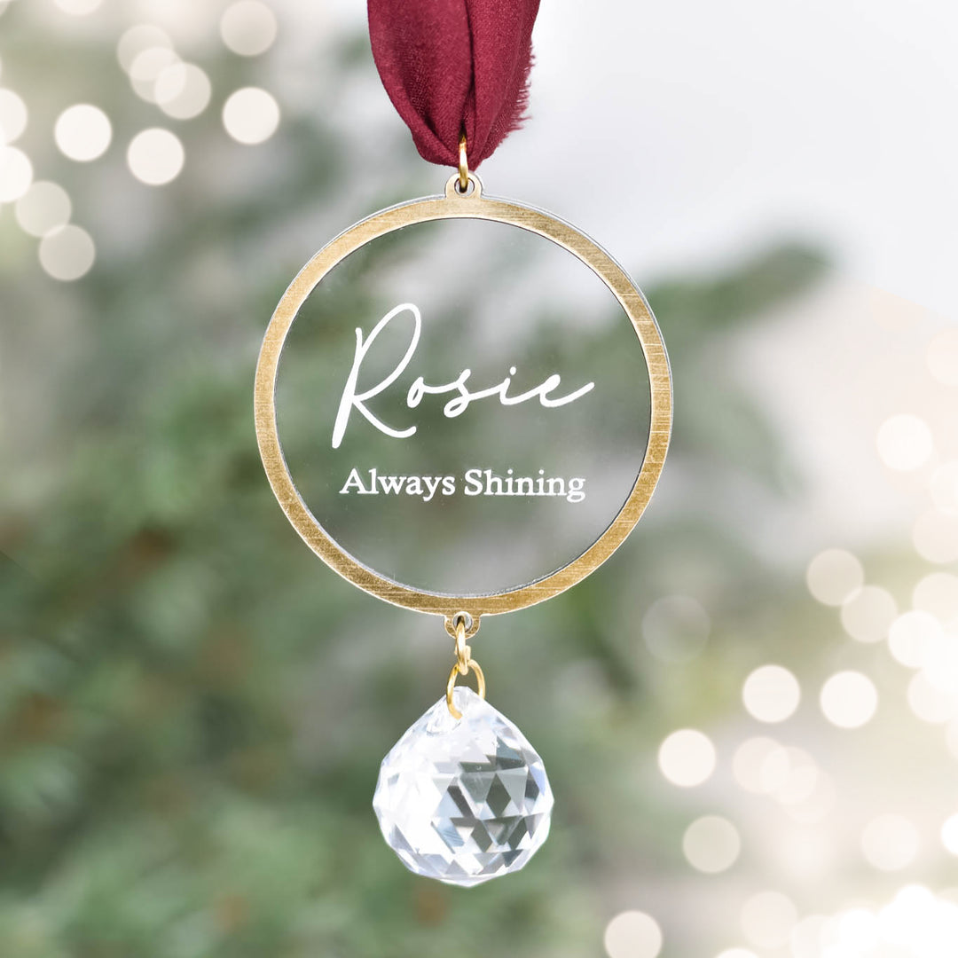 Always Shining Sun Catcher Ornament with gold circle, clear engraved name 'Rosie', and crystal drop, hanging with maroon ribbon.