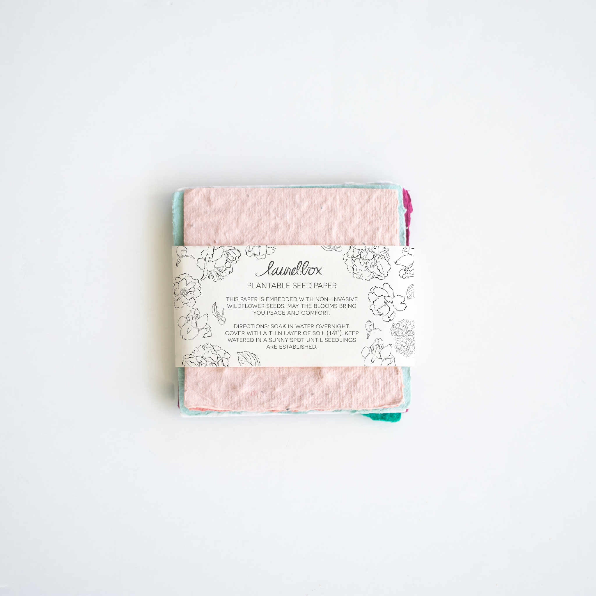 photo of pastel square pieces of paper in multiple colors stacked on top of one and other with a with label holding them all together that displays"laurelbox Plantable Seed Paper"