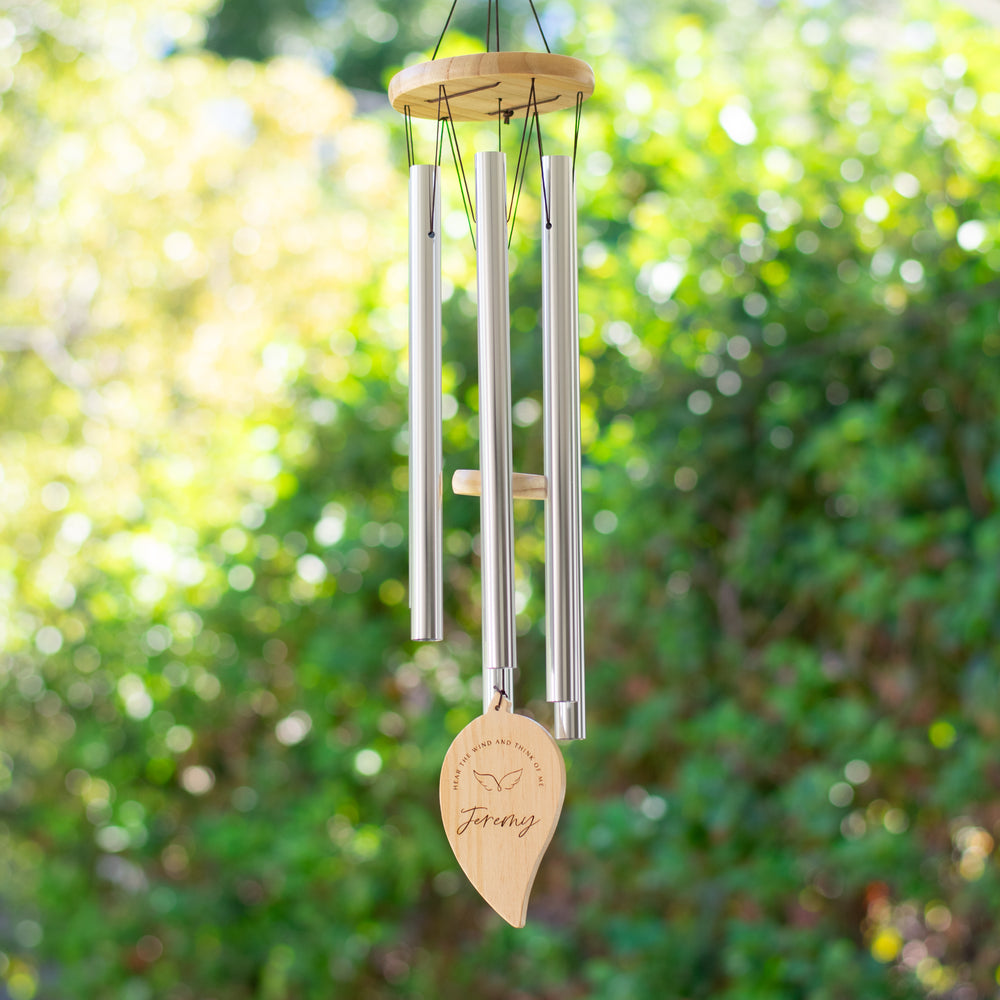A wind chime handing outdoors features long metal tubes with a wooden disc at the top. A wooden leaf is at the bottom with the text Jeremy and Hear the wind and think of me